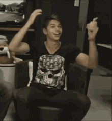 a man wearing a skull shirt is sitting in a chair .