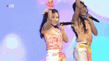 two women singing into microphones with the word live in the corner