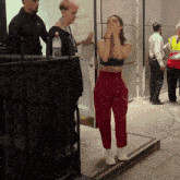 a woman in a black bra and red pants stands in front of a man in a yellow vest
