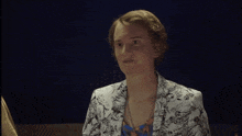 a woman wearing a floral jacket and a necklace looks at the camera