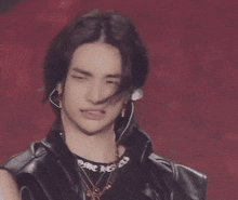 a close up of a young man wearing a leather jacket and earrings making a funny face .