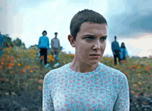 a girl with a very short haircut is standing in a field of flowers