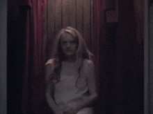 a woman in a white dress sits in a dark room
