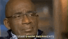 a bald man wearing glasses and a blue jacket is talking to the camera .