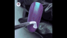 a close up of a purple nail being painted with white paint
