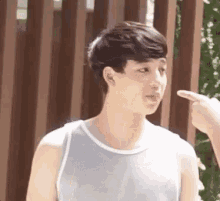 a young man in a tank top is pointing at another person 's finger .