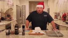 a man wearing a santa hat and an airway shirt stands in a kitchen