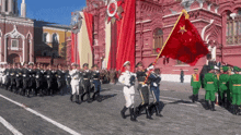 a group of soldiers marching in a parade with a red flag