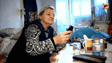 an elderly woman is sitting at a table with a remote control and a can of aquafina water .