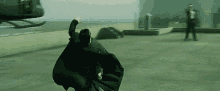 a man in a cape is running in front of a helicopter in the matrix .