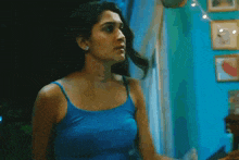 a woman in a blue tank top is standing in a room looking out a window .