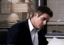 a man in a suit and tie is sitting at a desk with a piece of paper in front of him .