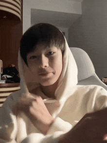 a young man wearing a white hooded sweatshirt looks at the camera