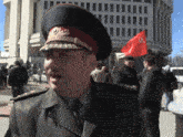 a man in a military uniform stands in front of a building with a red flag