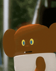 a brown teddy bear with yellow eyes is holding a white object
