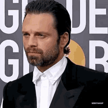 a man with a beard wearing a suit and white shirt is standing in front of a sign .