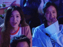 a group of people are sitting in a dark room watching a game and one woman is covering her mouth with her hand .