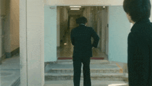 a man in a suit stands in a hallway looking at another man