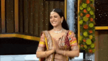 a woman in a sari is smiling and clapping her hands in front of a flower arrangement .