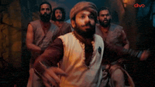 a man with a beard is standing in front of a group of men and says wait what ?