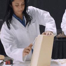 a woman in a white coat is working on a piece of foam