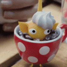 a red cup with white polka dots and a yellow figurine in it