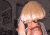 a woman wearing a blonde wig is talking on a cell phone in front of a mirror .