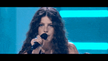 a woman is singing into a microphone with a blue background