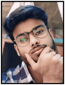 a man with glasses and a beard holds his hand to his chin