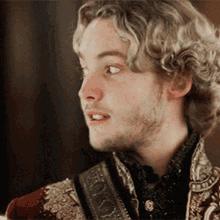 a young man with blonde hair and a beard is wearing a red jacket