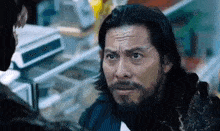 a man with long hair and a beard is talking to another man .