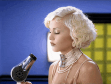a woman wearing pearls and a choker holds a hair dryer