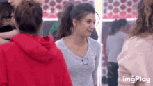 a group of women are standing next to each other in a room and one of them is wearing a red hoodie .