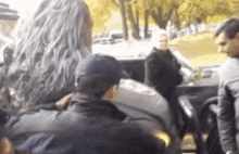 a group of people are standing around a car and talking to each other .
