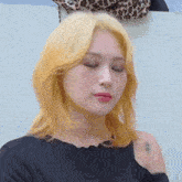 a woman with blonde hair is wearing a black shirt and making a funny face with her eyes closed .