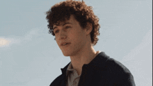 a man with curly hair wearing a blue and white shirt smiles