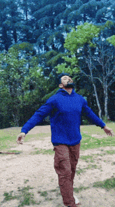 a man wearing a blue sweatshirt and brown pants is standing in a field with his arms outstretched