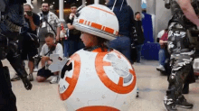 a little girl is dressed as bb-8 from star wars and wearing a helmet on her head .