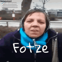 a woman wearing a hooded jacket and a blue scarf has the word fotze written on her face