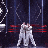 two men in white shirts are dancing on a stage with a star in the background