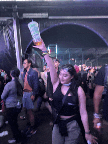 a woman holds up a cup with a straw that says ' iced tea ' on it in a crowd of people