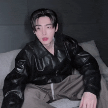 a young man wearing a black leather jacket and pants sits on a couch