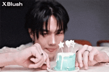 a young man is sitting at a table eating a small blue cake with candles .