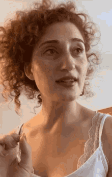 a woman with red curly hair and freckles is wearing a white tank top