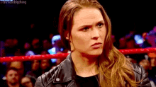 a woman in a leather jacket is standing in a wrestling ring with a crowd behind her .