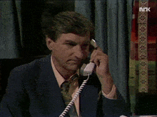 a man in a suit is talking on a telephone with the letters nk on the bottom right