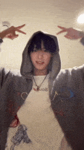 a young man wearing a hoodie and a necklace is making a peace sign with his hands .