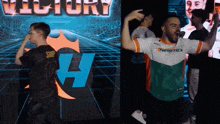 a man wearing a shirt that says energetics is standing in front of a screen that says victory