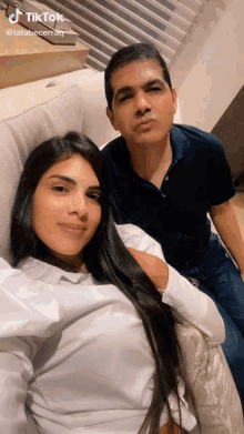 a man and a woman are posing for a picture on a couch with tik tok written on the bottom