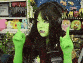 a woman with green paint on her face and green gloves is wearing headphones and giving the middle finger .